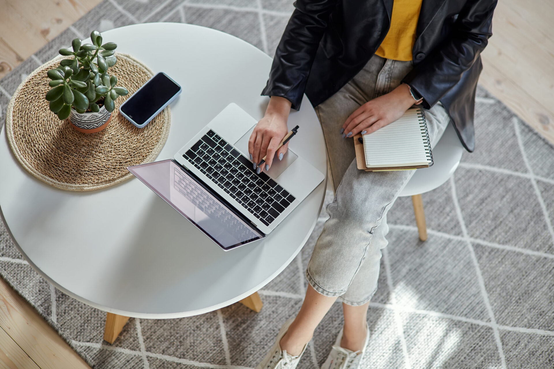Young woman using laptop and making notes in notebook sitting at workplace at home, remote work top view.